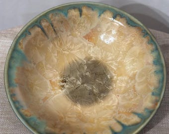 May include: A ceramic bowl with a light brown interior and a teal blue rim. The bowl has a unique, textured surface that resembles a crystalline pattern.