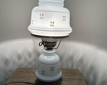 May include: A white table lamp with a floral design on the base and shade. The shade has a scalloped edge and the base has a decorative metal foot.