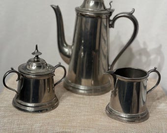 May include: A silver tea set with a teapot, creamer, and sugar bowl. The set has a traditional design with ornate handles and lids.