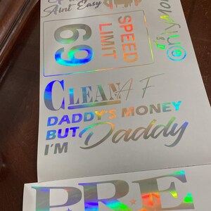 May include: A set of five iridescent vinyl stickers with various phrases and designs. The stickers include "Pimpin' Aint Easy", "Speed Limit 60", "Clean AF", "Daddy's Money But I'm Daddy", and "PRE Paper Route Empire".