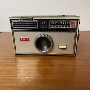 May include: A handmade wooden sign with the text "Welcome" in a playful font. The sign is painted white with a distressed finish, and features a decorative floral design in shades of pink and green. It measures approximately 12 inches wide.