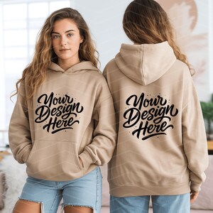 May include: A tan hoodie with a front pocket and a hood. The front of the hoodie features the text "Your Design Here" in a black script font. The back of the hoodie also displays the same text. The hoodie is worn by a person.