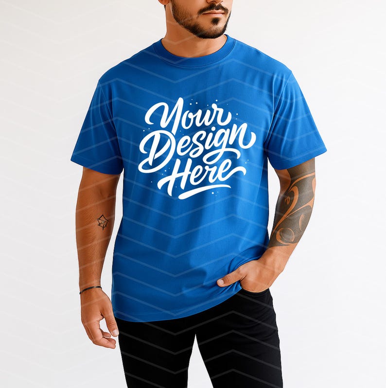 May include: A blue t-shirt with the text "Your Design Here" in white script. The shirt is short-sleeved and has a crew neck. The model is wearing black pants.