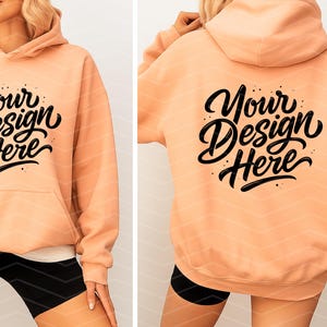 May include: Peach-colored hoodie with a front pocket and hood. The front and back of the hoodie feature the text "Your Design Here" in a black, stylized font. The hoodie is worn with black shorts.