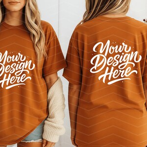 May include: Rust-colored t-shirts with the text "Your Design Here" in white script. The shirts have a relaxed fit and are displayed on a person. The back of the shirt also features the same text. The shirts are a blank canvas for custom designs.