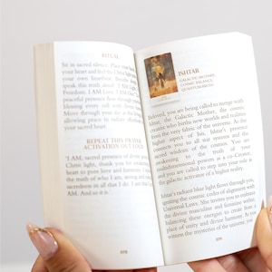 May include: An open book with text and an image of a woman with a golden aura. The text includes the words "Ishtar, Galactic Mother, Cosmic Balance, Quantum Birth" and a prayer. The book is held open with a hand.