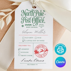 Puede incluir: Una etiqueta de regalo con el texto "North Pole Post Office" en escritura verde, con un sello rojo de Papá Noel. La etiqueta está atada a un regalo envuelto con una cinta y un lazo blancos. La etiqueta incluye el nombre "Olivia Miller".