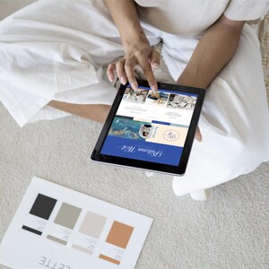 May include: A person is using a tablet to view a website called "Brillante Media". The website features a blue and white color scheme and includes images of various products. The tablet is on a white surface.