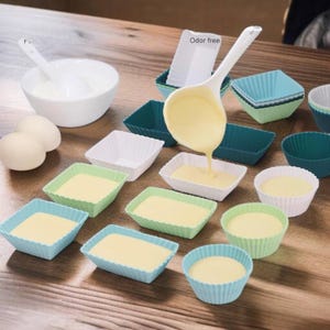 May include: A set of silicone baking molds in various colors, including white, green, and blue. The molds are in different shapes, including squares and rectangles. The molds are filled with a yellow batter and the text "Odor free" is visible in the image.