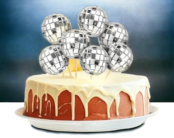 May include: A white frosted cake with red cake filling decorated with silver disco ball cake toppers.