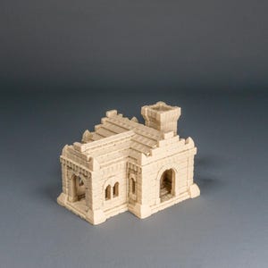 Può includere: Un edificio in miniatura beige con porte ad arco, finestre rettangolari e una piccola torre. Il modello ha una superficie strutturata, probabilmente per giochi da tavolo o modellismo.