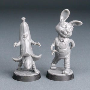 May include: Two gray miniature figurines. One is a person in a banana costume, the other is a rabbit wearing overalls. Both figures are on black circular bases. The Wargame Wonders logo is visible in the lower left corner.