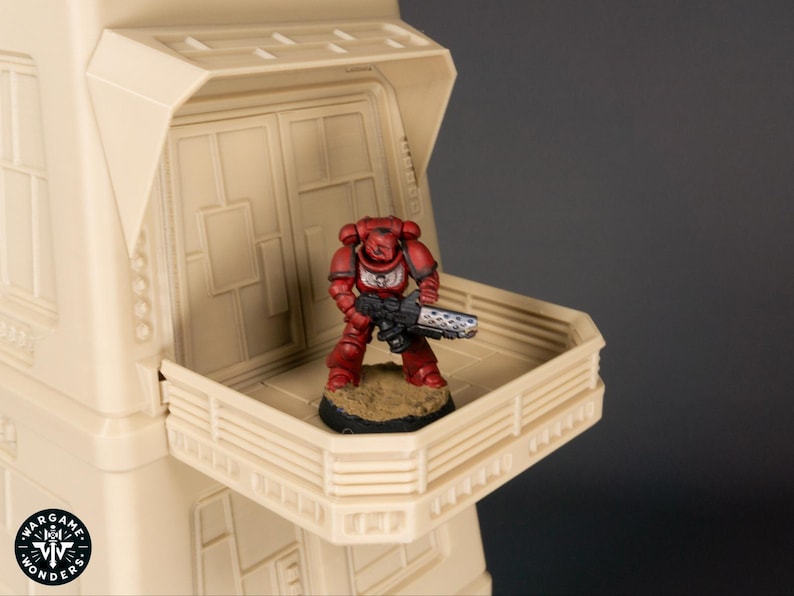 May include: A red and silver painted miniature space marine figure stands on a beige balcony with a railing. The figure is holding a gun and is standing on a small base.