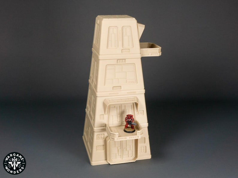 May include: A beige, multi-level building with a balcony and a small, red figure standing on the balcony. The building is made of plastic and is a miniature model.