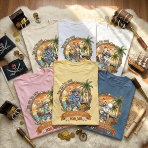 Pu&ograve; includere: Una collezione di magliette colorate con disegni a tema pirata. Ogni maglietta presenta un'illustrazione di un pirata animale all'interno di una cornice circolare, con i testi "Yo Ho Ho!" e "A Pirate's Life For Me". Le magliette sono disposte su una superficie bianca e soffice.