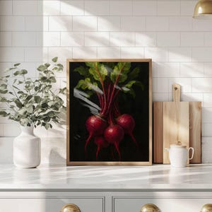 Puede incluir: Una impresión artística enmarcada que presenta una naturaleza muerta de remolachas. La pintura representa varias remolachas rojas vibrantes con hojas verdes y rojas sobre un fondo oscuro. La obra de arte se exhibe sobre una encimera blanca.