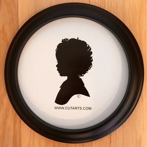 May include: A black and white silhouette of a child's profile in a black oval frame. The silhouette is of a child with curly hair. The frame has a white background with the text "www.cutarts.com" printed at the bottom.