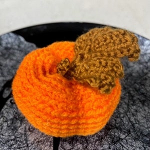 May include: A crocheted orange pumpkin with a brown crocheted stem.