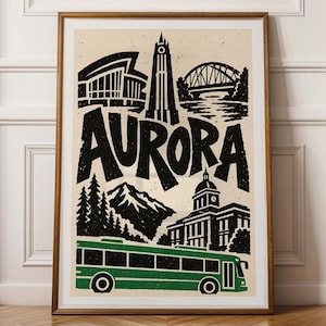 May include: A framed art print featuring a black and white illustration of the city of Aurora with the word AURORA in large bold letters. The design includes a bridge, a tall tower, mountains, trees, a building, and a green bus.