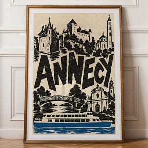 Puede incluir: Un póster enmarcado con una ilustración en blanco y negro de la ciudad de Annecy, con la palabra ANNECY en letras negras grandes. La obra muestra un castillo, un puente y una iglesia, con un barco azul flotando en el agua en la parte inferior.
