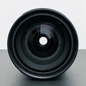 May include: A black camera lens with multiple concentric rings and a central glass element. The lens has a wide aperture and a reflective surface, suggesting it is designed for capturing light and images.
