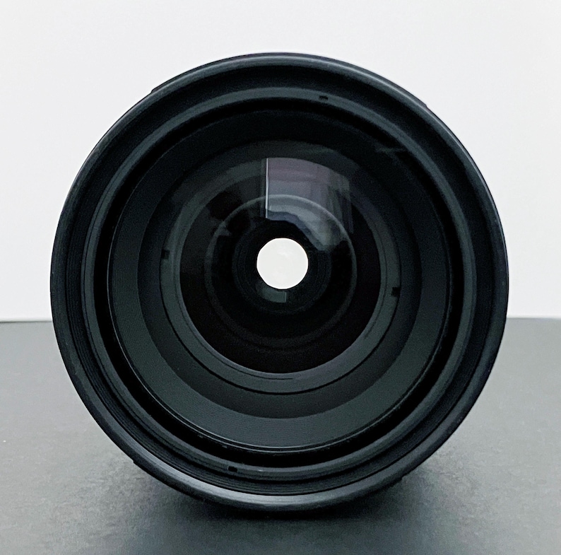 May include: A black camera lens with multiple concentric rings and a central glass element. The lens has a wide aperture and a reflective surface, suggesting it is designed for capturing light and images.