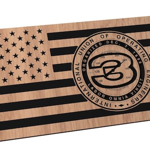 May include: A wooden American flag with a black and white logo in the center. The logo is a circle with the text "International Union of Operating Engineers Organized Dec. 7, 1896 Labor Omnia Vincit" around the outside. The logo also features a compass with a number 3 in the center.