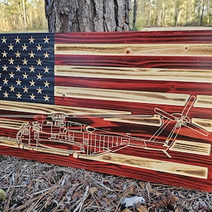 May include: A wooden American flag with a red, white, and blue color scheme. The flag has a helicopter silhouette burned into the wood.