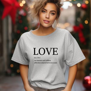 May include: A light gray t-shirt with the word "LOVE" printed in black, along with its definition. The definition reads: "An intense and selfless affection shared between souls."