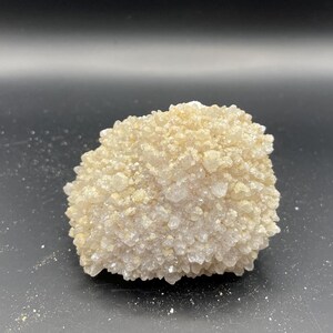 May include: A cluster of small, white and light brown crystals, forming a rounded, irregular shape. The crystals are densely packed together, creating a textured surface.