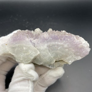 May include: A cluster of amethyst crystals with a light purple hue. The crystals are arranged in a cluster, with some of the crystals pointing upwards. The crystals are translucent and have a glassy luster.