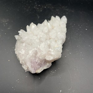 May include: A cluster of white quartz crystals with a hint of purple. The crystals are clustered together in a natural formation.