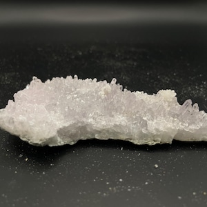 May include: A cluster of pale purple amethyst crystals with a rough, natural texture. The crystals are arranged in a jagged, irregular shape, resembling a small mountain range.