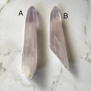 May include: Two amethyst crystal points, labeled A and B, on a white background. The crystals are both clear and have a light purple hue.