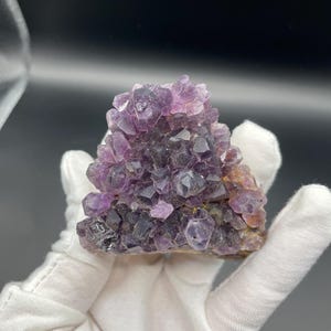May include: A cluster of purple amethyst crystals with a rough, natural texture. The crystals are arranged in a pyramid shape, with the largest crystal at the top.