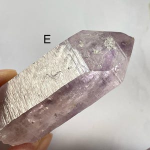 May include: A large, light purple amethyst crystal point with a smooth, polished surface. The crystal has a natural, slightly cloudy appearance and is pointed at both ends.