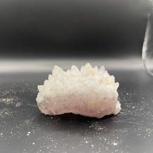 May include: A cluster of clear quartz crystals with a pink base. The crystals are arranged in a pointed, spiky formation.