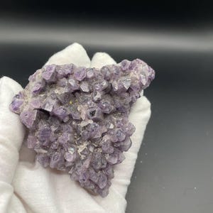May include: A cluster of purple amethyst crystals with a rough, natural texture. The crystals are densely packed together, creating a unique and eye-catching display.