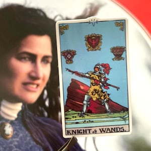 May include: A tarot card with a blue background and a knight riding a horse with a red cape. The card is titled "Knight of Wands".
