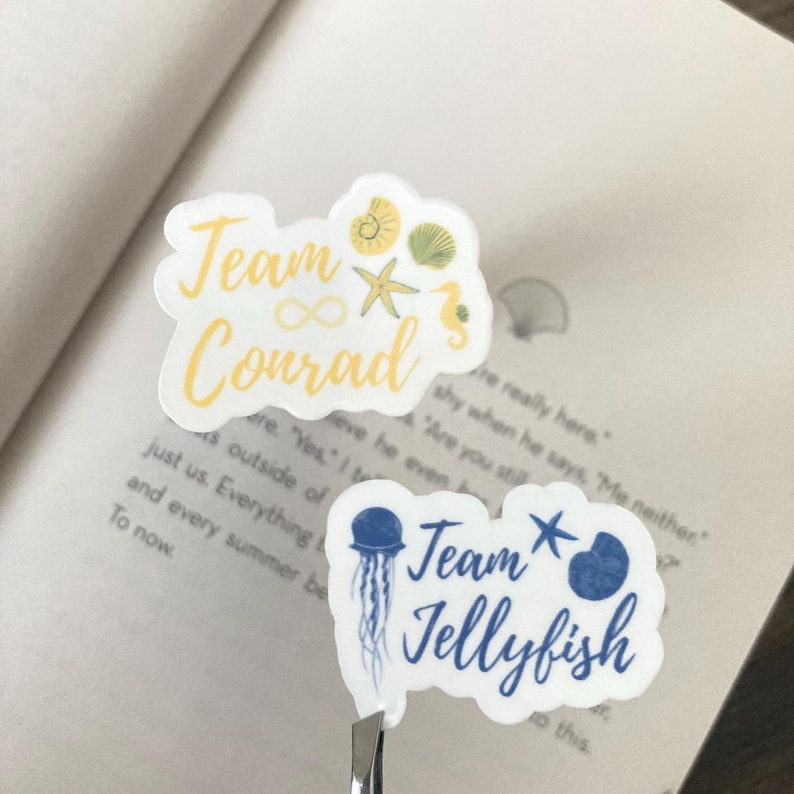 May include: Two white stickers with blue and yellow accents. The top sticker says "Team Conrad" with an infinity symbol and a starfish. The bottom sticker says "Team Jellyfish" with a jellyfish and a starfish.