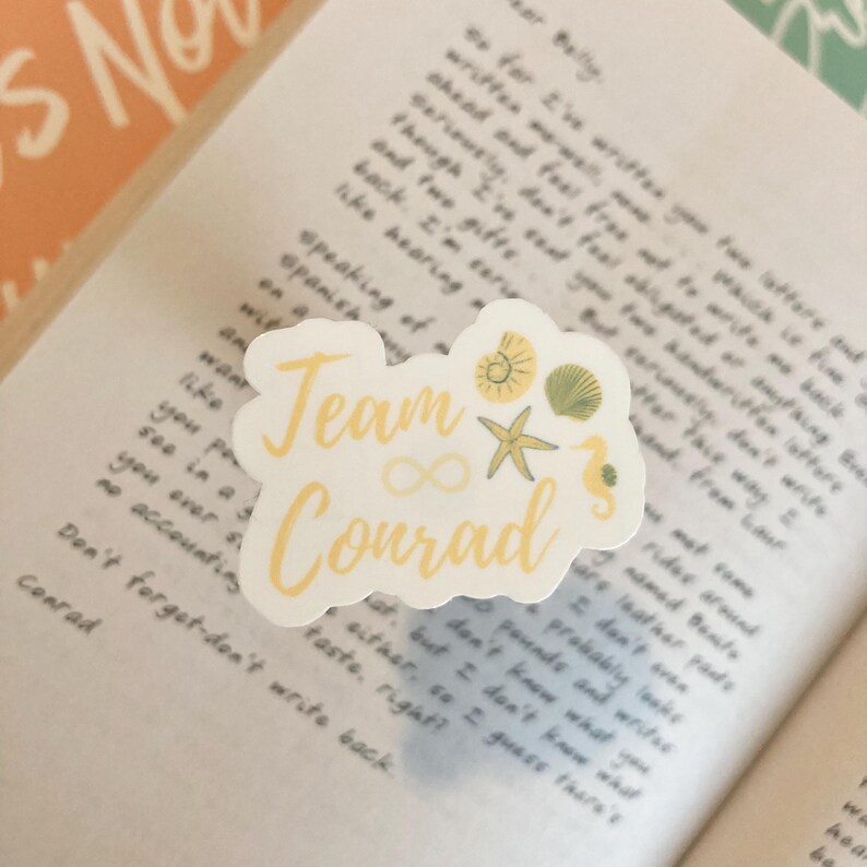 May include: A white sticker with the text "Team Conrad" in yellow lettering. The sticker features a yellow infinity symbol, a yellow starfish, a yellow seashell, and a yellow seahorse.