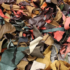 May include: A collection of leather offcuts in a range of colours, such as brown, tan, red, green, and black. The pieces are of different sizes and shapes, indicating they are leftovers from a leathercraft project. The image is well-lit, showing the textures.