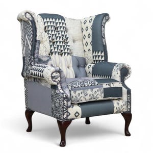 May include: A patchwork armchair with a high back and rolled arms. The chair is upholstered in a mix of patterned fabrics in grey, white, and black. It has dark brown wooden legs and a buttoned back, typical of a wingback chair.