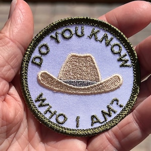 May include: A green embroidered patch with the text "Do you know who I am?" and a brown cowboy hat in the center.