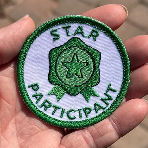 Könnte beinhalten: Ein gestickter Aufnäher in Grün und Weiß mit dem Text "STAR PARTICIPANT" und einem grünen Stern in einem grünen Stern.