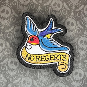 May include: Embroidered iron-on patch featuring a blue bird and a yellow banner that reads "NO REGRETS".