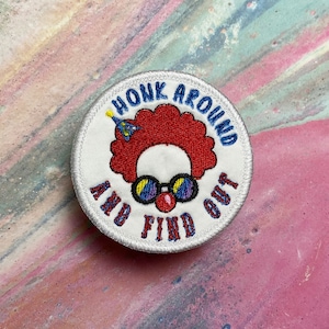 May include: White embroidered patch with a red-haired clown wearing blue sunglasses and a party hat. The text around the clown reads "Honk Around And Find Out".