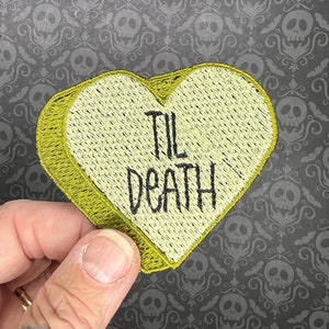 May include: A yellow heart-shaped patch with the text "TIL DEATH" embroidered in black thread.