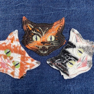 May include: Three embroidered cat face patches. One is black and orange, one is white and black, and one is orange and white.