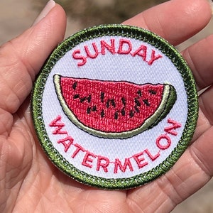 Könnte beinhalten: Ein grüner und weißer gestickter Aufnäher mit dem Text "SUNDAY WATERMELON" in rosa Schrift. In der Mitte des Aufnähers befindet sich eine rote Wassermelonen-Scheibe mit schwarzen Kernen.